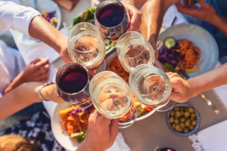 six wine glasses, two filled with red wine four filled with white, come together in a cheers over an out of focus dinner table