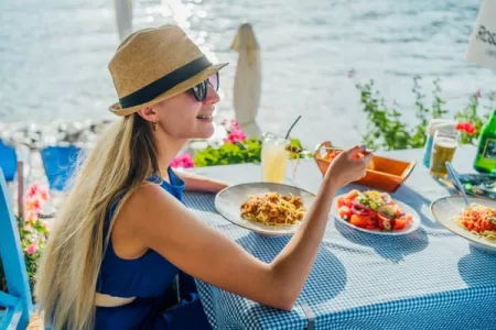 a woman in a straw hat enjoys a plate of pasta by the ocean