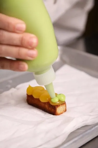 a chef squeezes green puree onto a dish