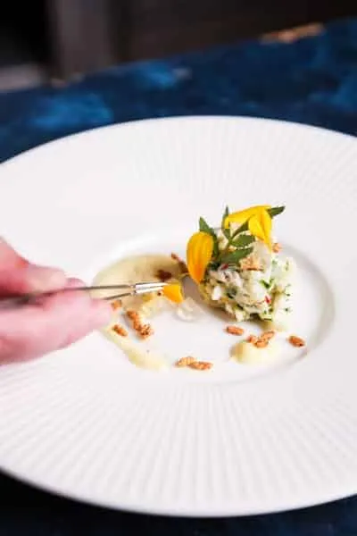 a chef uses tweezers to place an edible flower petal on a dish