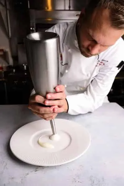 Chef Barry Tonkinson uses a silver canister to pipe foam onto a plate