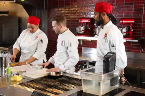 Chef Barry Tonkinson oversees Advanced Contemporary Cuisine & Technique students wearing red commis hats
