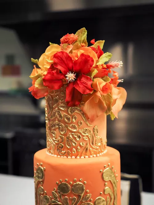 Orange cake with gold detail and orange and red gumpaste flowers from the ICE Professional Cake Decorating program