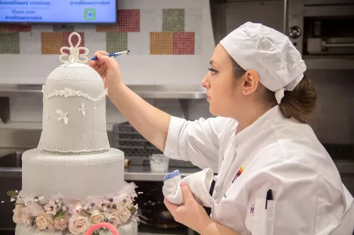 A student puts the finishing touches on a graduation cake in the ICE Professional Cake Decorating program