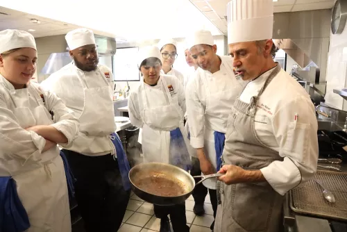 ICE Chef-Instructor Herve Malivert holds a saute pan while speaking to a class of ICE students