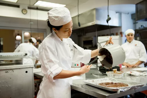 An ICE pastry student scrapes melted chocolate from a robot coup