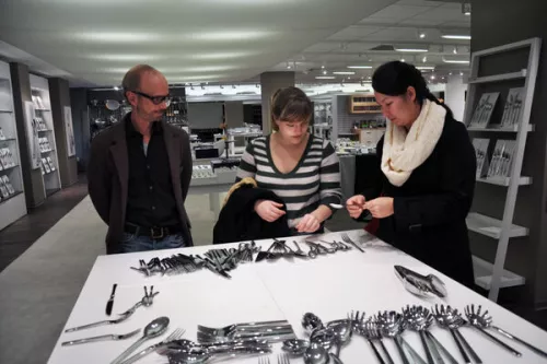 Two women and an older man choose silverware at a showcase room during a Tourism, Travel & Hospitality Mangement field trip