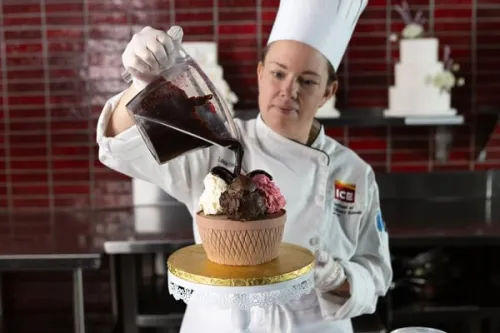 ICE Pastry Chef Louisa pouring melted chocolate over a cake on a stand.