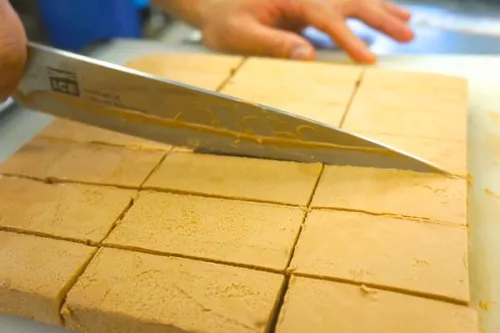 Close up view of hands holding chefs knife with ICE label slicing dough. 