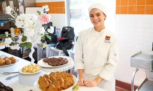 An ICE student in chef's whites smiles at a pastry buffet