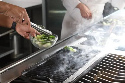 a culinary nutrition student places boy choy on a hot grill