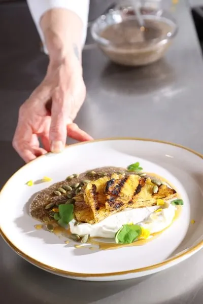 a chef pushes a plate forward composed of grilled pineapple, yogurt and chia seeds from ICE' Culinary Nutrition curriculum