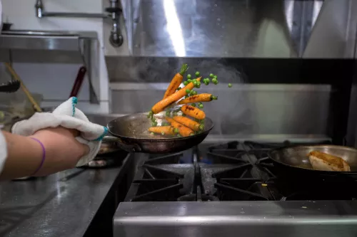 Culinary school student flips a saute pan full of carrots and peas