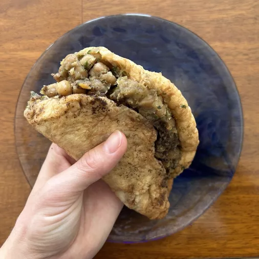 Hand holding a doubles - flatbread with chickpea filling