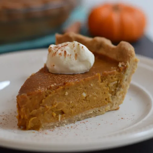 Slice of pumpkin pie topped with whipped cream on a plate