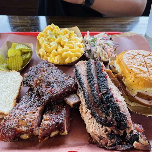 A plate of barbecued meats, bread, coleslaw, pickles and mac and cheese