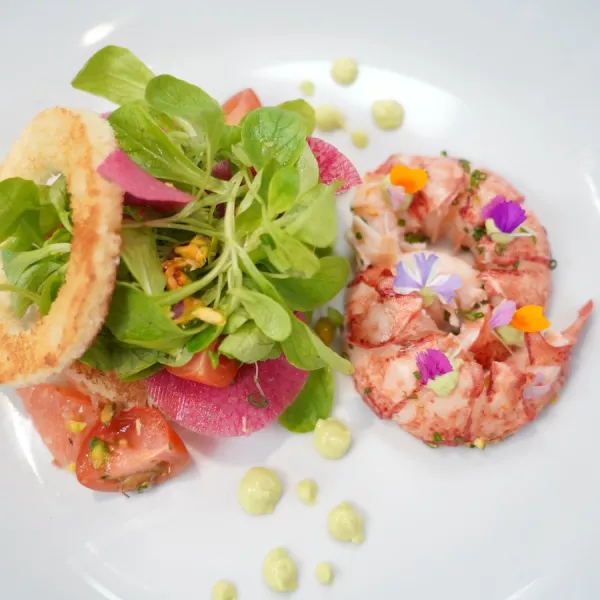 A green salad with colorful vegetables sits on a white plate next to red lobster