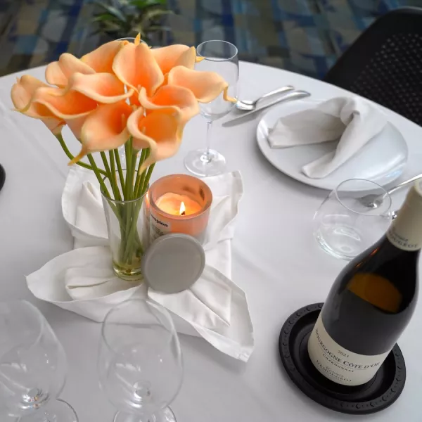 A table set with a white tablecloth, orange flowers, a candle and a bottle of wine