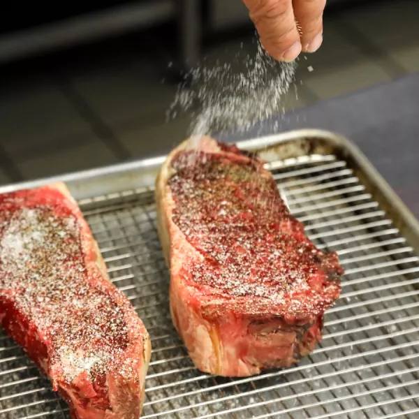 A hand seasons steak on a metal tray