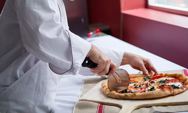 A culinary student slices a pizza.