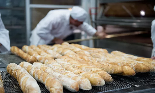 An ICE bread baking student reaches into the oven to pull out fresh bread, with baguettes in the foreground