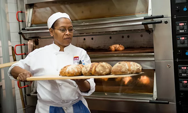 An artisan bread baking culinary student removes loaves from oven.