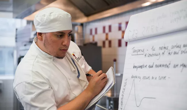 A pastry arts student takes notes during class in culinary school at the Institute of Culinary Education