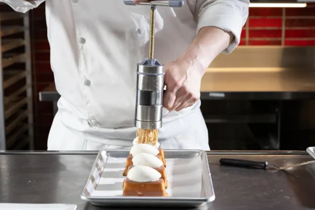 an Advanced Pastry & Baking Technique student finishes a Mont Blanc dessert with a hazelnut mousse extruder