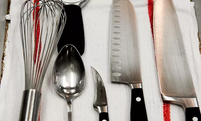 A set of tools, including a whisk, tasting spoon, and various knives, that students use in culinary school