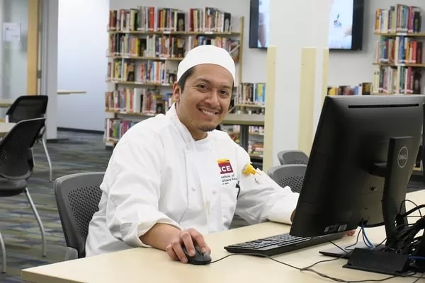 ICE student in chef coat and had smiles while studying at computer.