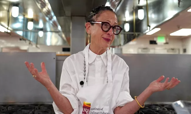 Chef Nancy Silverton wears an apron that reads "Institute of Culinary Education" and talks to ICE students in a kitchen