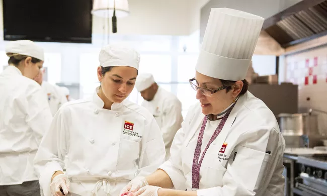 An ICE chef instructor demonstrates a technique to a culinary school student