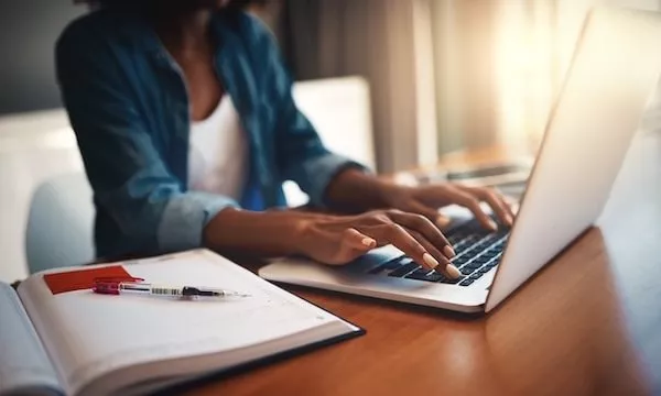 An ICE student types on a keyboard with her open notebook on the desk beside her. 