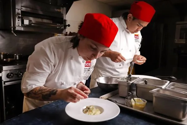 two Advanced Contemporary Cuisine & Technique students add finishing details to their plated dishes