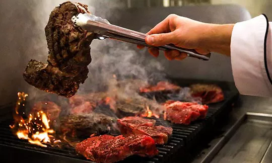 A chef cooks steak on a fired up grill.