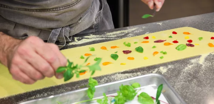 Hands pressing colorful leaves of herbs and petals of flowers on pasta dough