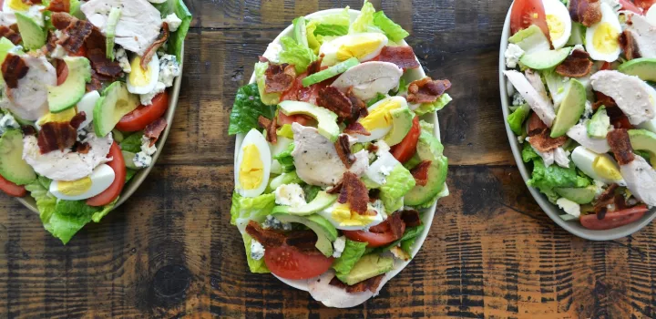 Three cobb salads sit on a wooden table