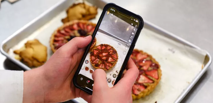 A student takes a photo of a strawberry tart dessert on their phone