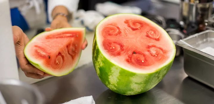 An instructor slices a watermelon open in a Health-Supportive Culinary Arts class.