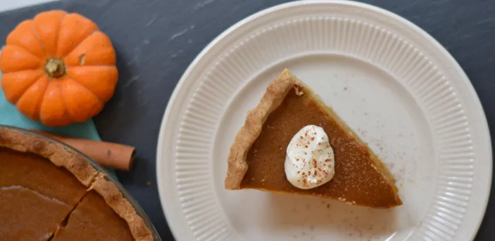 Slice of pumpkin pie topped with whipped cream on a plate