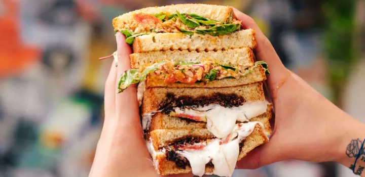 Hands holding two sandwiches cut in half stacked on top of eachother