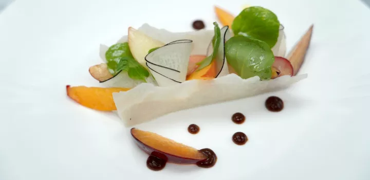 A stone fruit summer salad with peaches, greens and jicama sits on a white plate