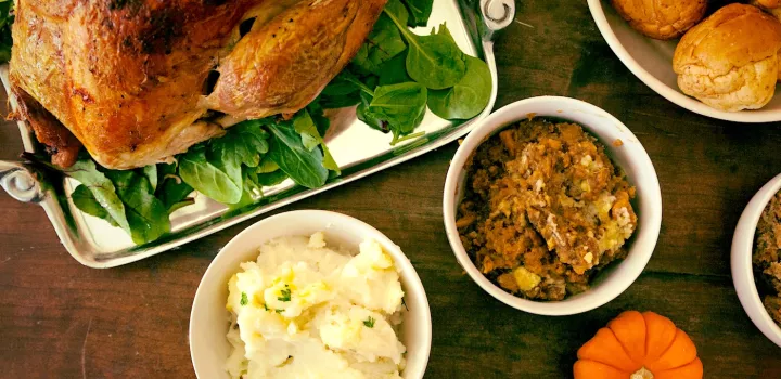 A roast turkey, mashed potatoes, sweet potato casserole and bread rolls in bowls on a wooden table