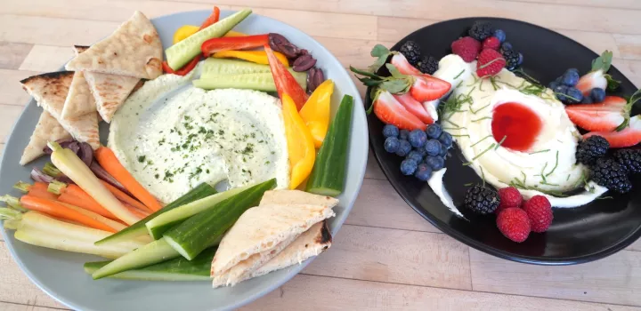 Two plates of whipped feta dip with vegetables and cut fruit