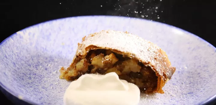 A piece of apple strudel sits next to whipped cream on a white plate