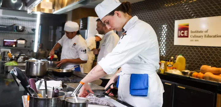 ICE student cutting a fish, two students cooking in the background