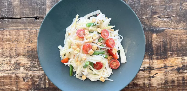 A bowl of fermented green papaya rice noodle salad on a wooden table