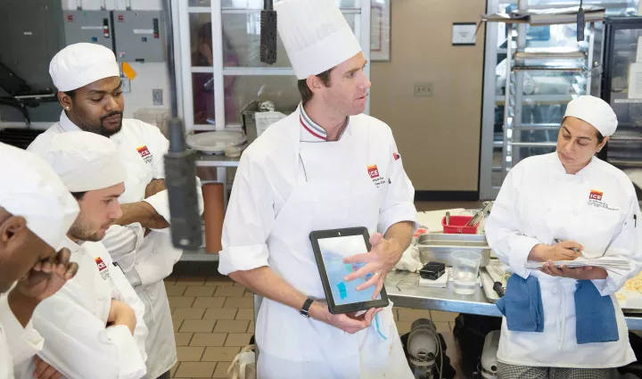An ICE chef instructor shows culinary school students something on an iPad in class at the Institute of Culinary Education