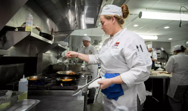 An ICE culinary arts student seasons food inside a saute pan at culinary school