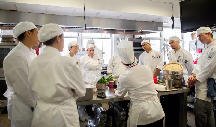 Culinary school students look on as an ICE chef instructor demonstrates a technique in class